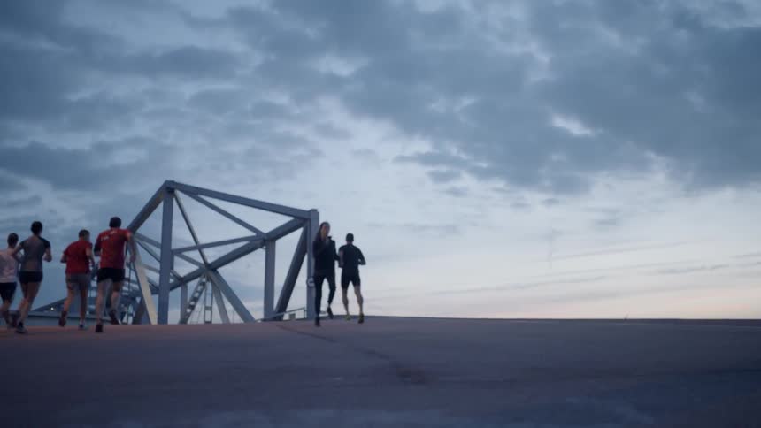 People jog through a bridge metal structure at sunset