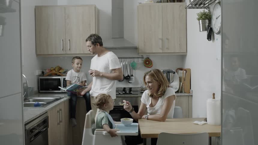 Woman feeds a child in a highchair and a man reads a book to a boy