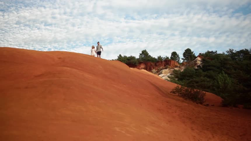 Man and woman hold hands and walk on hilly sandy landscape