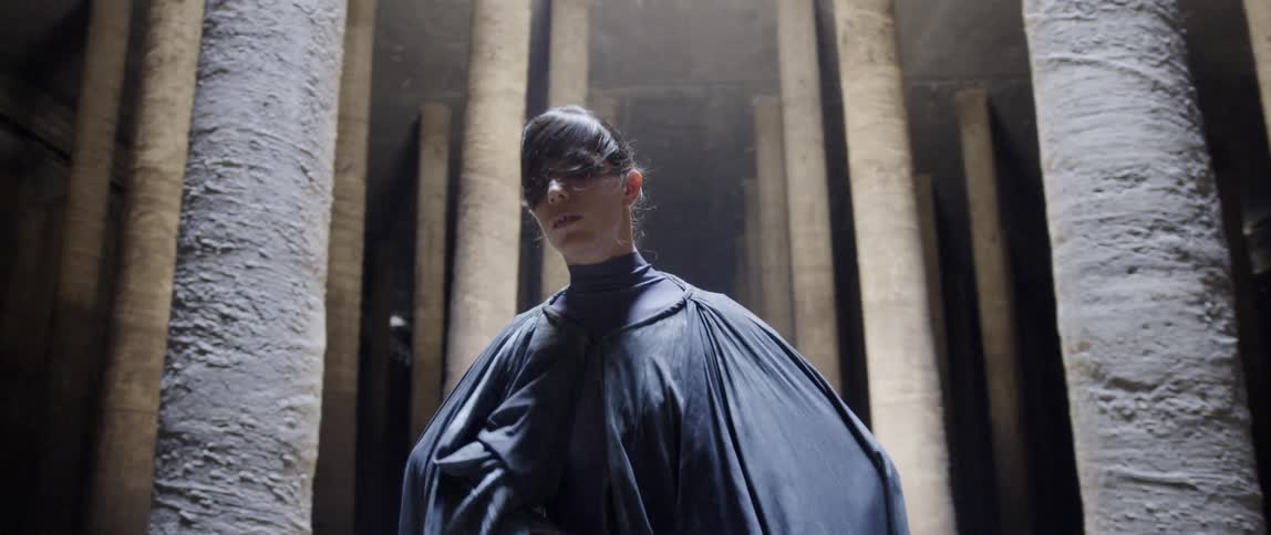 Person wearing a black cape dances near pillars