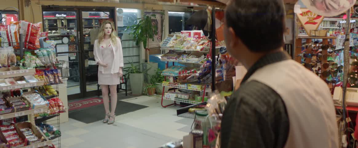 Man working at a convenience store behind the counter stops and looks at a woman