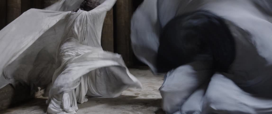 Two people wearing white and black capes wave their capes and dance