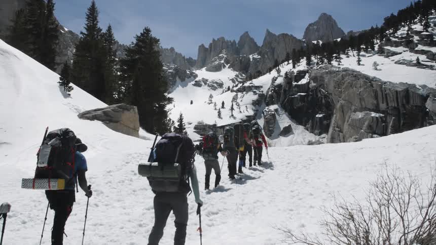 Group of people are hiking up snow covered mountain on sunny day