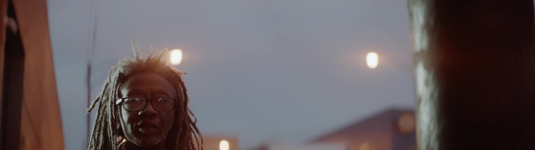 An older man is walking outside in a city at dusk