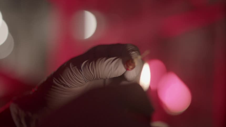 Person with gloved hands lights a needle with a lighter