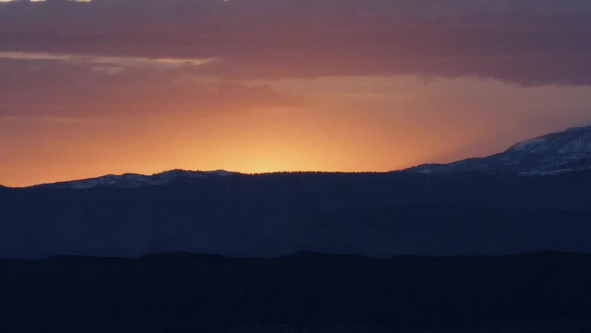 Sun sets behind hills on a cloudy evening