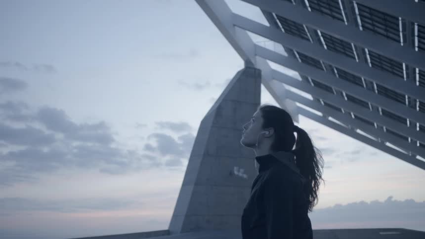 Woman stands underneath a metal structure at sunset