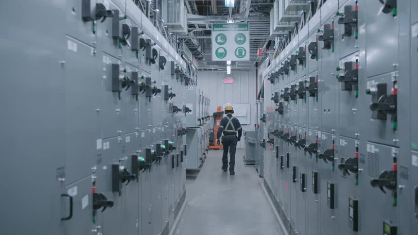 Man wearing a helmet walks down a hallway in a factory