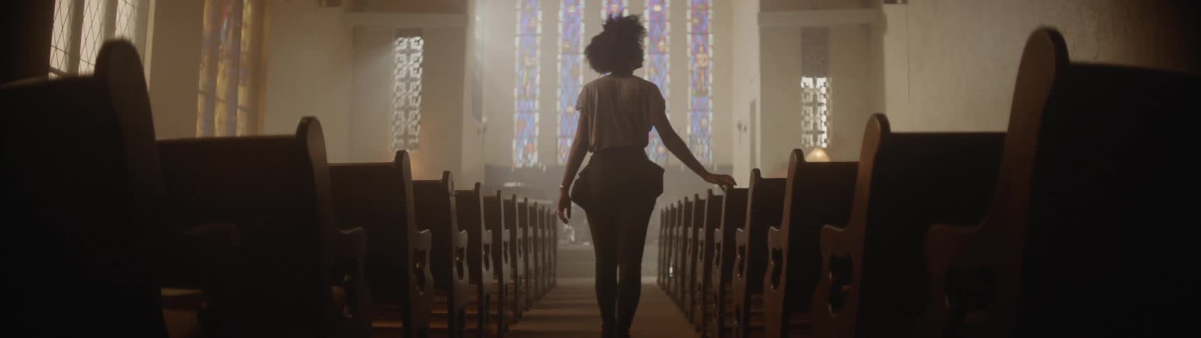 Woman walks in an aisle in between rows of church pews