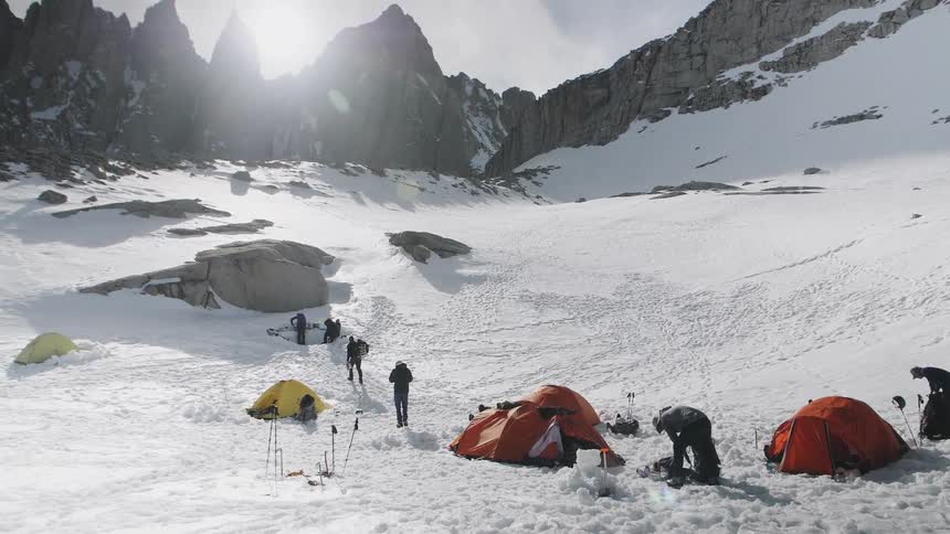 Group of people camp at the bottom of snowy mountains