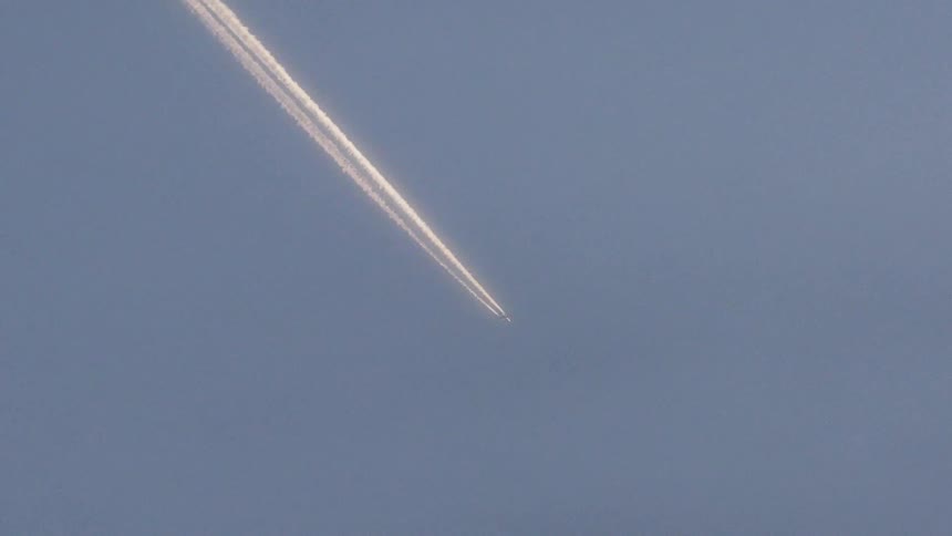An airplane is leaving a vapor trail as it flies in the sky on a sunny day