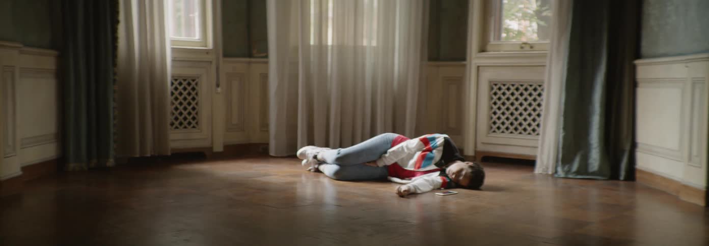 A young person lays on the floor next to their phone