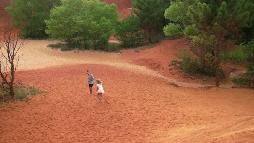 Man and woman run on a sandy beach near trees