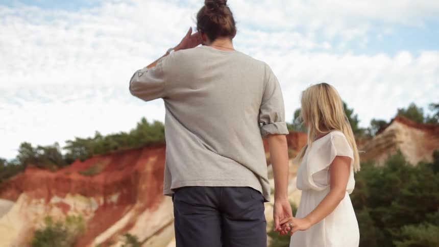 Man and woman hold hands as they stand under a cloudy blue sky