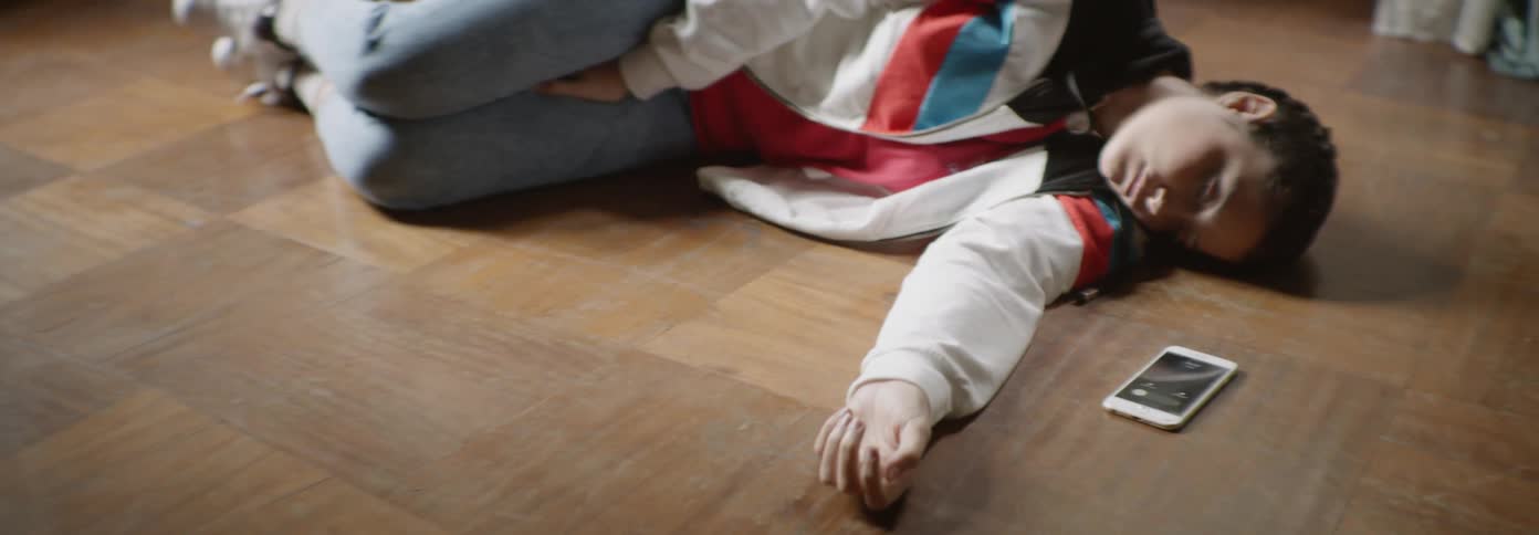 A young person lays on the floor next to their phone