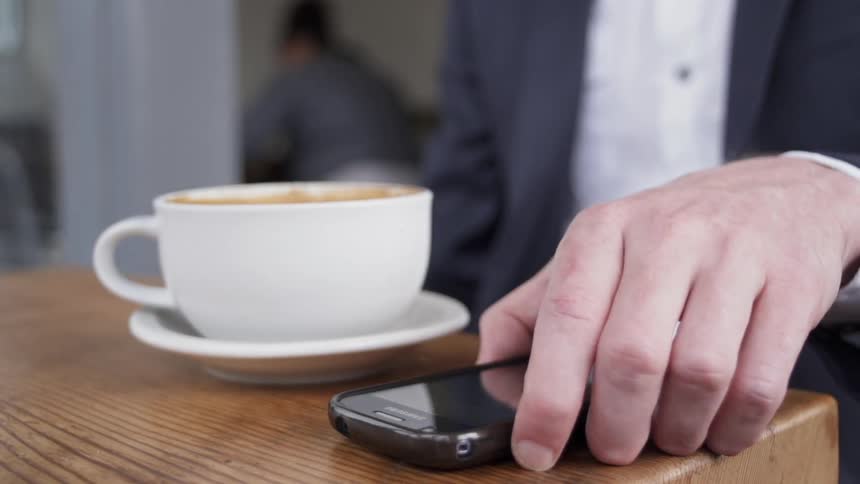 A man picks up his phone while drinking coffee