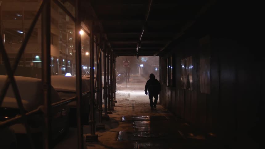A man walks down a wet city sidewalk at night