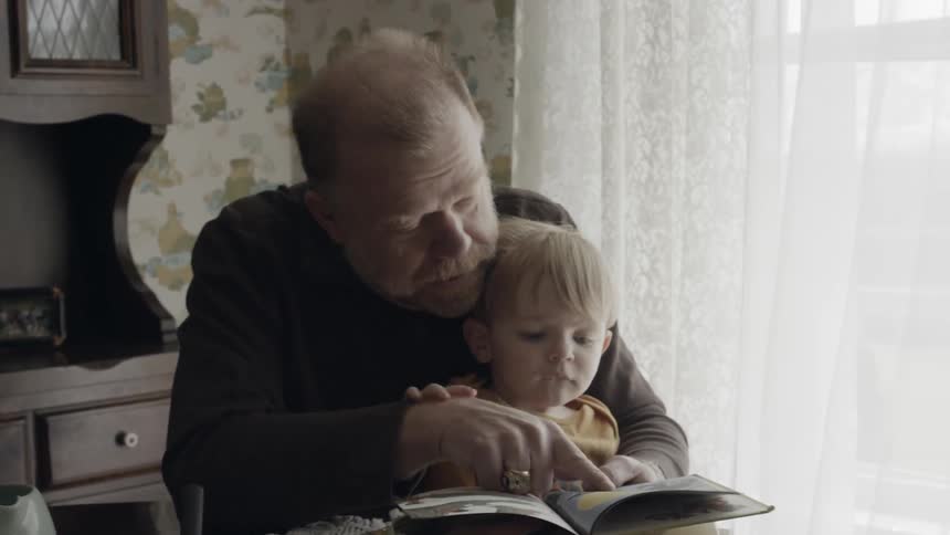 Grandfather is reading book to grandson at table