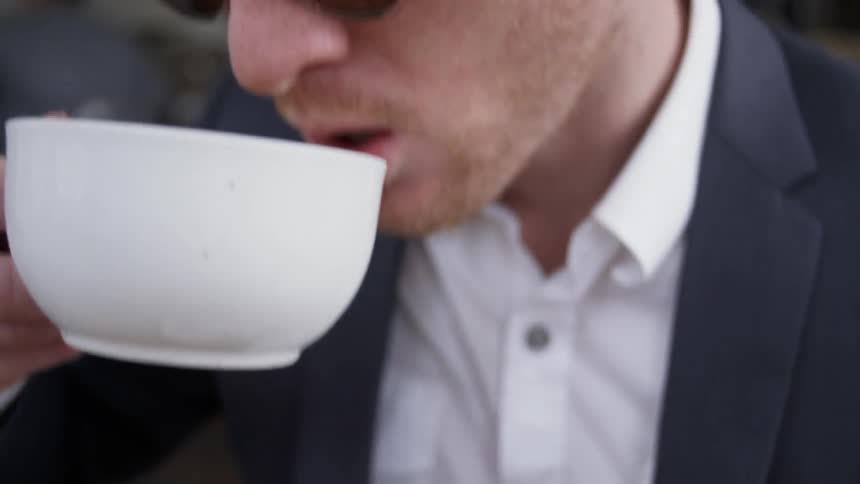A cappuccino is sitting on a table in front of a man in daylight