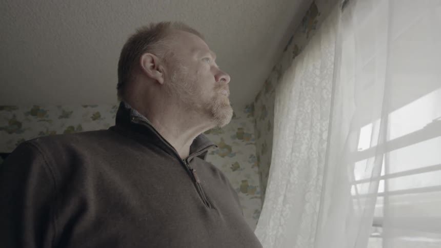 Man holding mug is looking out open window on windy day