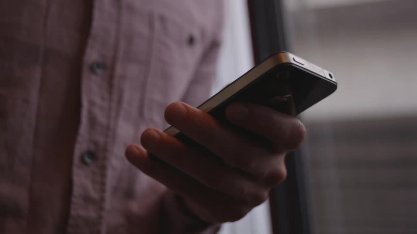 A person on a moving train leans against the door and looks at their phone