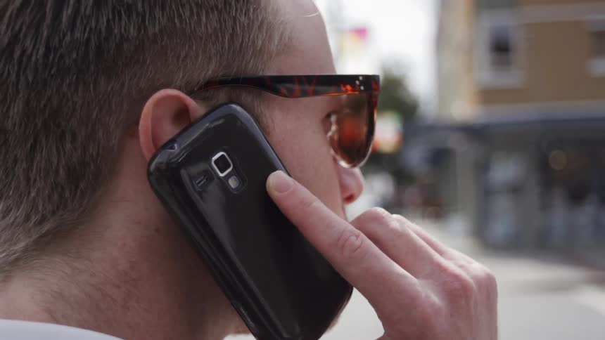 Man wearing sunglasses holds a cellphone to his ear