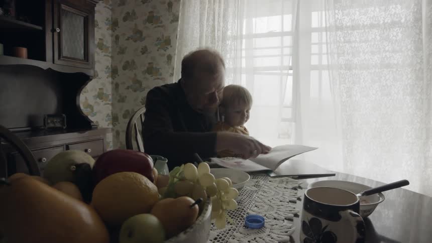 A man sits a table holding his grandson and reading to him