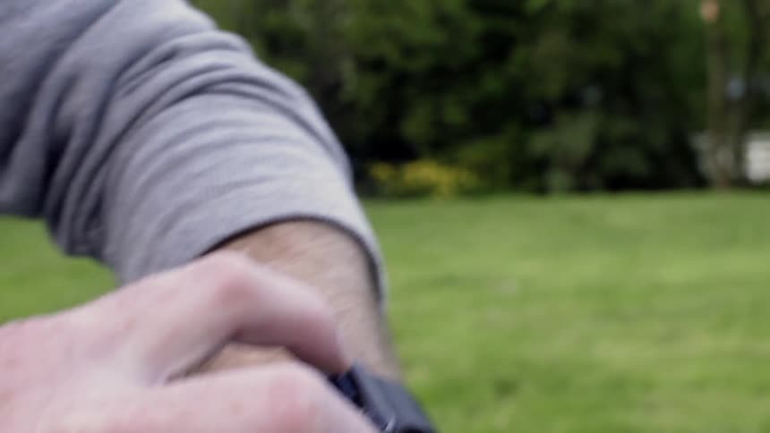 A man is setting his smartwatch as he walks outside in a park during daylight