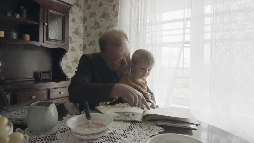 Grandfather and grandson are reading book at dining room table