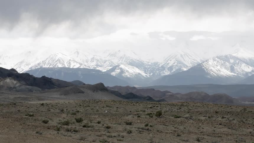 Clouds roll over snowy mountains and grassy plains