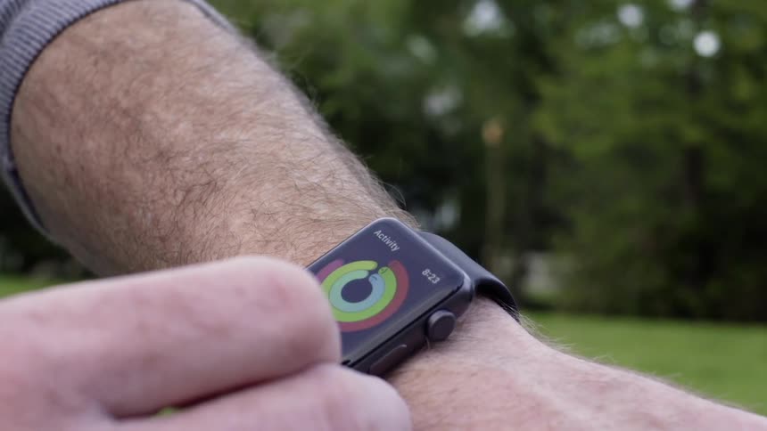 A man is checking his smartwatch outside in a park during the day
