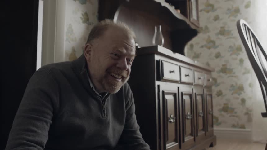 An elderly man laughs and gestures on the floor