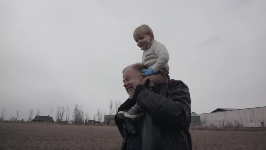 A boy rides on his grandfather's shoulders on a cloudy day