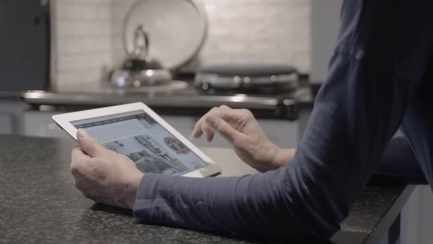 A woman at the kitchen counter scrolls on a tablet