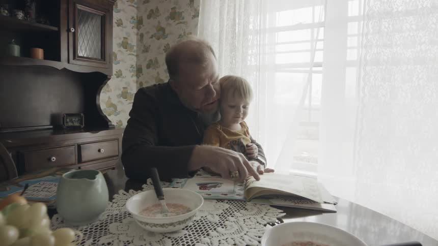 A man reads a book to a young boy at a table