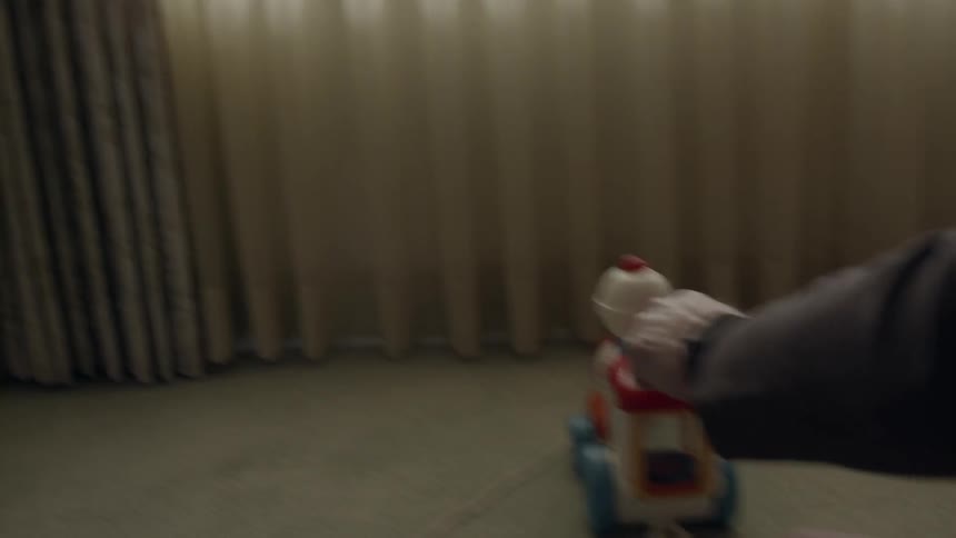 A toddler boy is playing with a toy inside a home in daylight with an old man