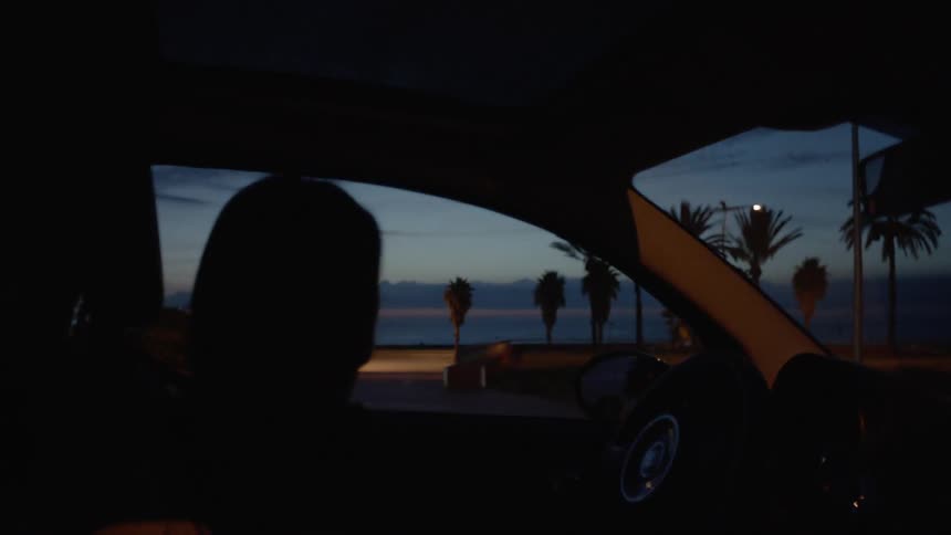 Woman sits in a parked car at dusk
