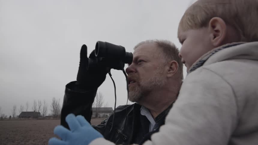 A grandpa is showing his grandson how to use binoculars outside in winter
