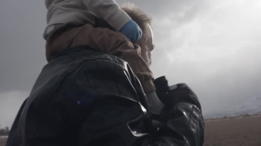 Elderly man walks with a child on his shoulders on a stormy day