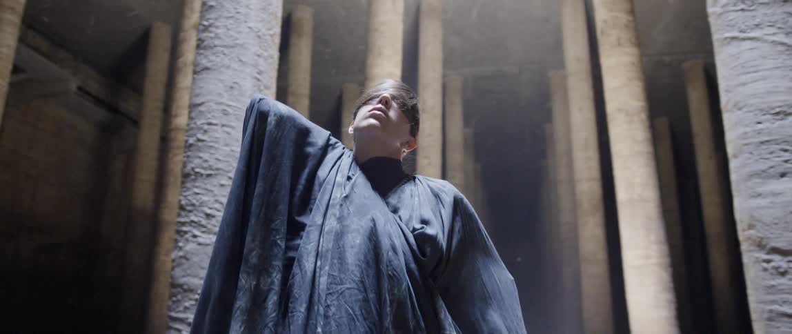 Person wearing a black cape dances near pillars