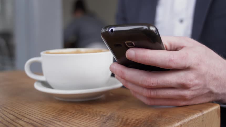Man scrolls on his cellphone as he sits at a table