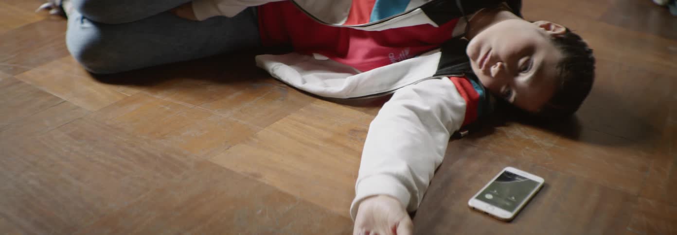 A person lays on the ground next to a phone