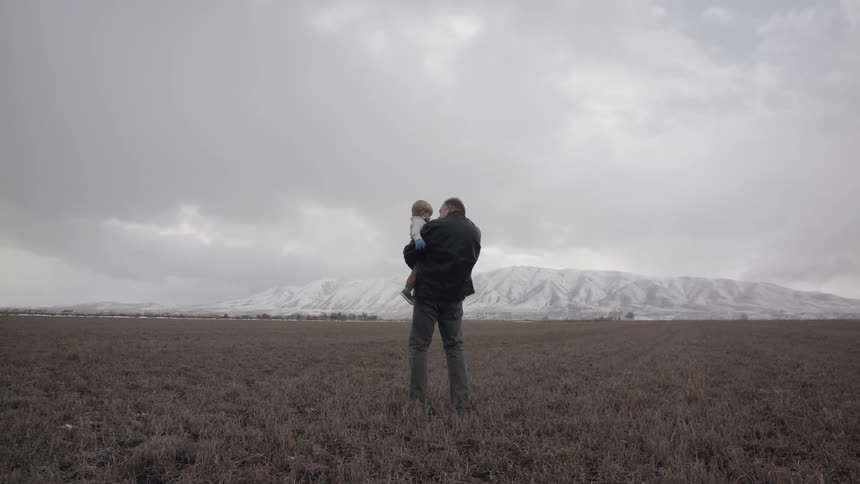 Man stands on mountain valley floor holding child