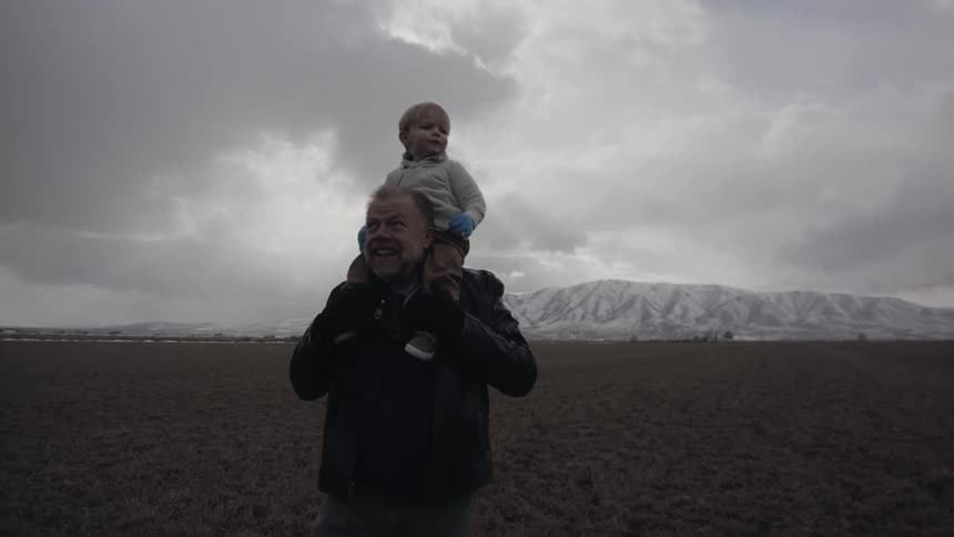 An old man is carrying a toddler on his shoulders outside on a stormy day