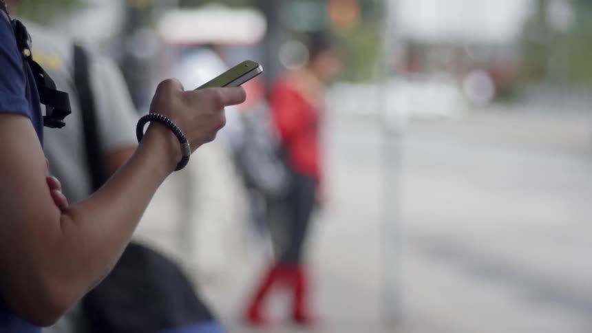 Person stands on a sidewalk looking at their phone