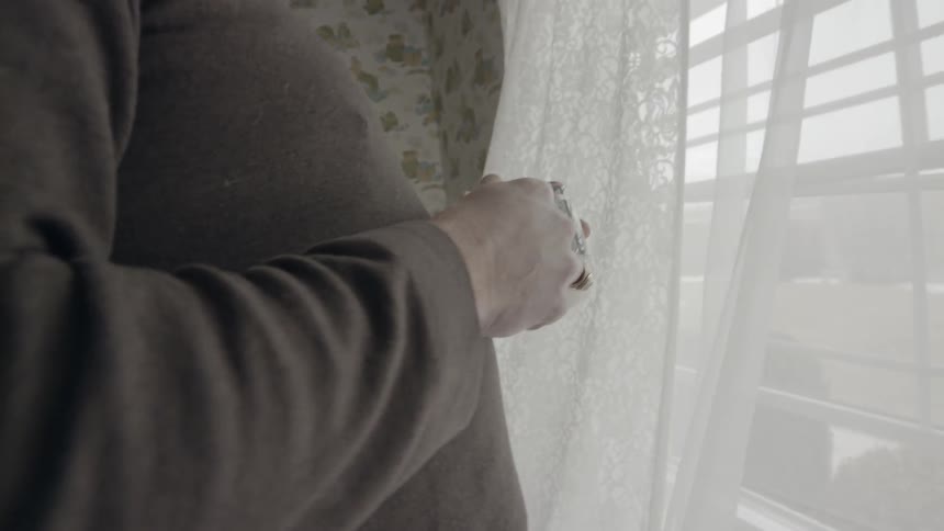 Man holding a mug is watching out his open window on windy day