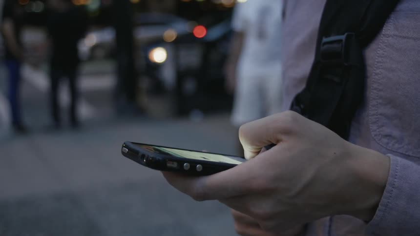 A person uses their phone while standing on a sidewalk