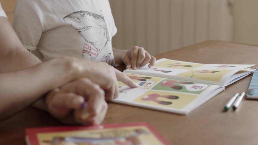 Adult and child sitting at a table looking at a book