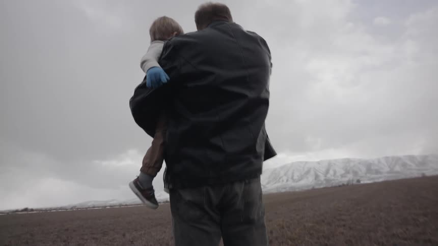 A man carries a young child through the field