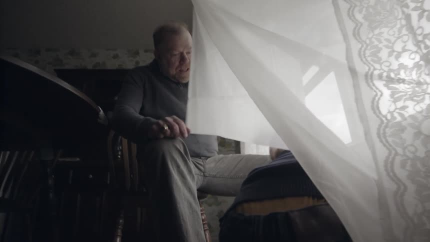 Toddler picks up a toy from behind a curtain as an elderly man watches